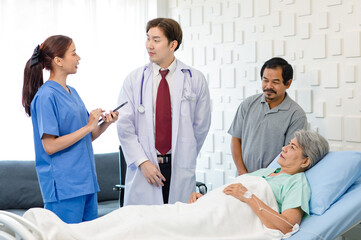Fototapeta premium Asian professional successful male doctor in white lab coat with stethoscope female assistant internship nurse in blue uniform holding tablet computer visiting old senior unhealthy patient in ward