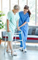 Fototapeta na wymiar Asian young professional successful friendly female nurse in blue hospital uniform helping supporting physical therapy senior old pensioner unhealthy injury woman patient walking via four legs walker