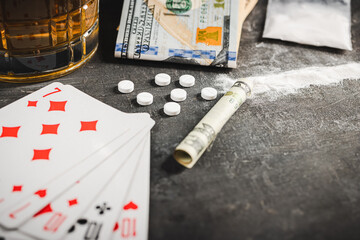 Playing cards for poker game, alcohol drink in a glass, white pills, powder drugs and US dollar...