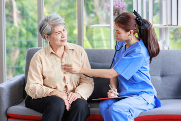 Obraz premium Asian professional successful female internship nurse in blue uniform sitting on sofa couch smiling using stethoscope listening to heart rate beating from old senior elderly pensioner woman patient