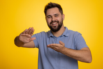 Young caucasian man showing wasting, throwing money around, more tips, big profit, winning lottery jackpot, successful shopping payment purchase, cashback. Guy isolated on studio yellow background
