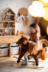 A little girl in a Scandinavian children's room on a horse. Game nursery with a canopy. Containers for storage of toys. Dollhouse.