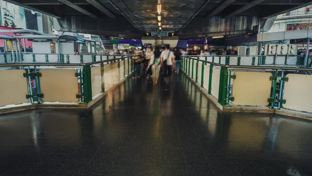 Fast motion of busy crowd of people walking in city in the evening. Moving people on BTS skytrain station skybridge in Bangkok city time lapse. Long exposure. Zoom out