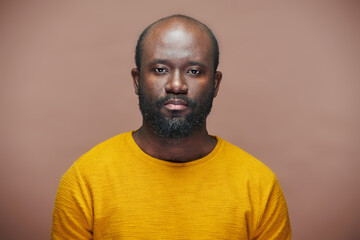 Portrait of African American man with stubble in yellow shirt looking at camera against brown background