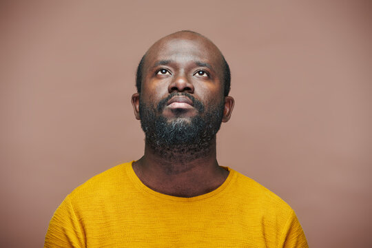 Portrait of African American man looking up with pensive expression standing against brown background