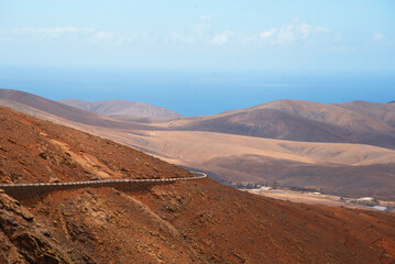Vista panorámica de un paisaje desértico y volcánico con un camino sinuoso a lo largo de la ladera de la montaña en el mirador de Las Peñas en Fuerteventura en un día soleado en las Islas Canarias.