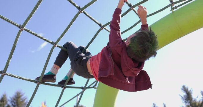Young boy climbing upside down on rope ladder at play strucutre park - dangerous play