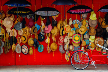 A variety of trendy and colorful hats hang on the red background of a roadside shop. Women's designer sun hats in different colors. Design of women's beach hats. Beach hats for the summer.