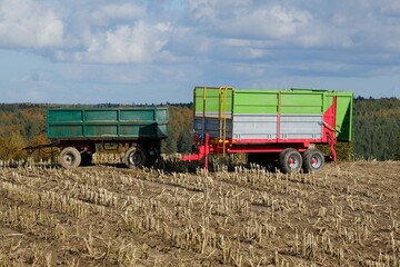 Two trailers stand in a field with cut corn in an autumn scenery