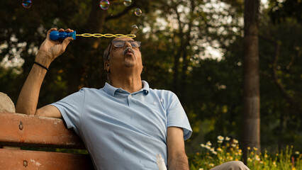 Fototapeta premium Senior citizen male in park playing with bubbles