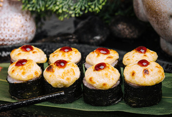 Served warm sushi rolled in nori sheets with ginger and wasabi on a black stone plate