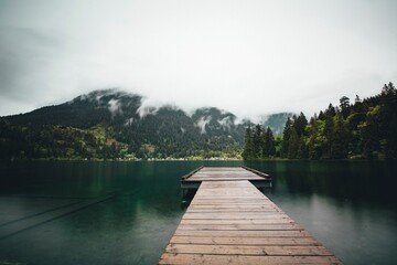 Wooden dock on a lake and a mountain of evergreen trees covered with mist