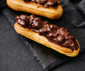Two eclairs with dark chocolate on black board
