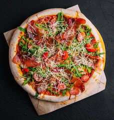 Italian pizza with prosciutto, arugula and tomatoes