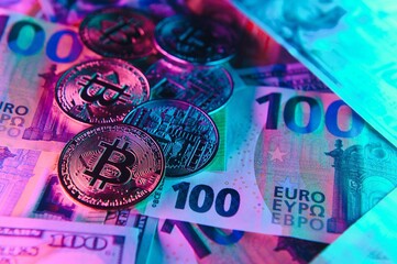 Close up heap of golden bitcoin physical coins on top of Euro, dollar banknotes background, high angle view, selective focus