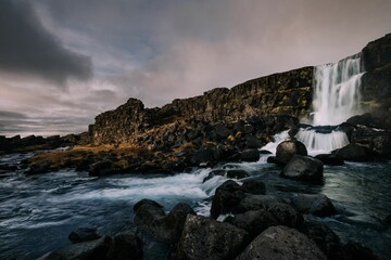 Beautiful landscape of Iceland with a waterfall against rocky cliffs in a cloudy weather