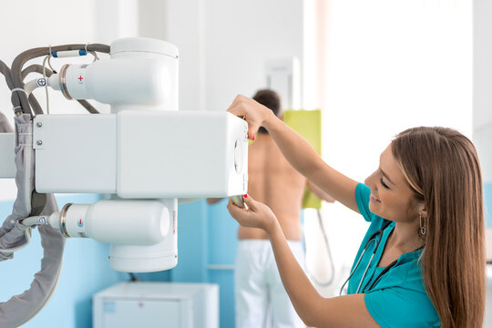 Hospital Radiology Room: Man Standing Topless Next to X-Ray Machine while Female Doctor Adjusts it. Healthy Patient Undergoes Medical Exam Scanning with the Doctor's Help.
