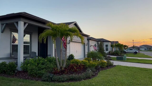 Facade of a beautiful house, with a front garden made up of palms, short grass and tropical plants, in Coral Ridge in Miami, driveway, sidewalk and street