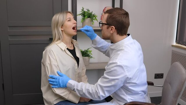 Doctor using inspection spatula to examine patient throat. ENT doctor doing throat exam of a woman. Patient opened her mouth to throat check-up