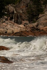 large rock formation next to beach with water crashing in it