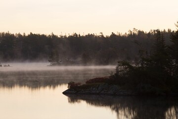 a boat floating on a lake in front of fogy forest