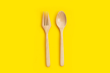 Wooden spoon and fork on yellow background.