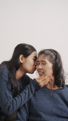 Kiss, Mother's day concept, young adult female daughter congratulate excited asian elderly mother at sofa with birthday anniversary, two generations family photo, real people.