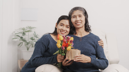 Gift, present, flowers, Mother's day concept, young adult female daughter congratulate excited asian elderly mother at sofa with birthday anniversary, two generations family photo, real people.