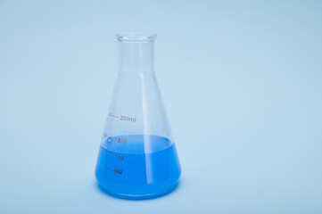 Still life with graduated flat bottomed lab flask with blue fluid solution, isolated over blue color background. Chemistry. Science, Clinical research. Healthcare and medicine concept. Horizontal shot