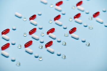 Medical background with red gelatin translucent capsules with essential oils, Omega 3 or fat-soluble vitamins and pharmaceutical pills laid out in pattern on blue surface. Pharma industry and business