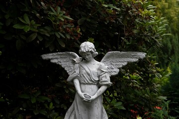 an angel statue stands in the grass with trees behind it