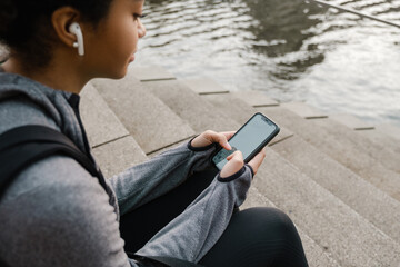 African girl using smartphone while sitting outdoors by the river