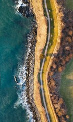 Aerial view over a road with rocky coast and forest trees by the ocean water