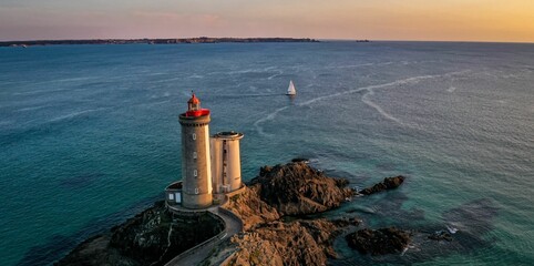 Obraz premium Aerial view of a beautiful seascape with a white lighthouse and a sailboat in the background