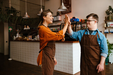 Man with down syndrome and his female colleague giving high five while standing in cafe