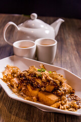 braised vegan beancurd tofu with minced pork meat and Japanese bonito flakes in thick golden sauce on wood table tea pot cup asian chinese halal food vegetarian banquet restaurant menu