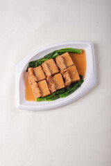 vegetarian braised beancurd with tofu puff and green vegetables in thick soy golden sauce on wood table asian Chinese halal food vegan banquet restaurant menu