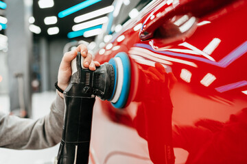 Professional vehicle polishing and detailing service in a modern car workshop. Brightly lit workspace with large led lights. High quality car valeting concept.