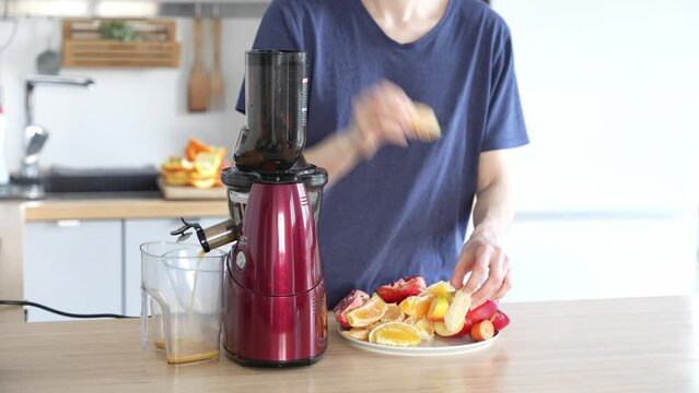 Caucasian woman making juice at home. Female puts fruits into low speed juicer. Apple, orange, carrot, granate. Healthy lifestyle. Morning juice. Squeeze juice.