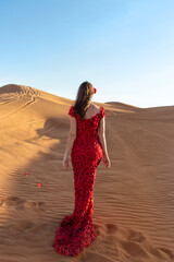 Young beautiful woman in long red dress with red rose petals among the desert. Desert rose conception