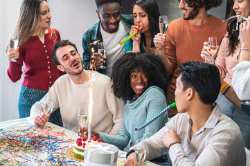 Group of friends celebrating a party and the festive young African American woman in the center, with cake and gift on the table in the foreground