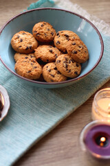 Books, reading glasses, e-reader, plate of chocolate pralines, bowl of cookies, cups of tea and lit candles on the table. Selective focus.