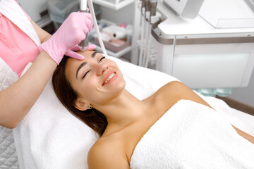 Obraz na płótnie Canvas Rejuvenating therapy,Skin resurfacing, facial muscles of the client are lifted and toned using a microcurrent machine by the esthetician at the beauty salon. Cosmetology service