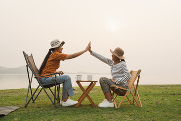Asian two teenager high five gesture while sitting at camping sunset. 