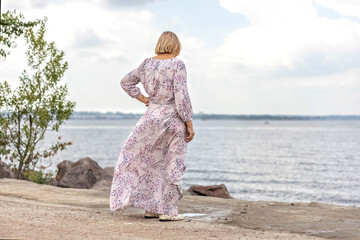An elderly woman in a long pink dress on the seashore. Gulf of Finland