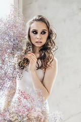 Fototapeta na wymiar A beautiful romantic young woman with makeup poses against a background of colorful gypsophila flowers. The concept of perfumery, cosmetics.Spring