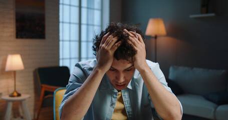 Image of tired young business man. Portrait of depressed young Asian man with head in hands sitting at home.