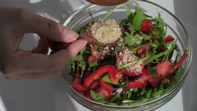 woman's hands skillfully sprinkle food yeast over a vibrant vegetable salad with a wooden spoon, showcasing the nutritional boost. Nutritional Yeast: A Flavorful and Nutrient-Packed Addition