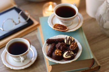 Plate of chocolate pralines, bowl of cookies, cups of tea, glasses of juice and lit candles on the table. Selective focus.