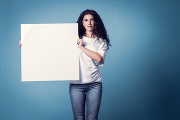 Fototapeta na wymiar Beautiful curly woman holding blank billboard isolated on blue background